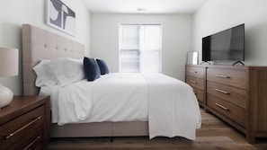 Ein modernes Schlafzimmer mit einem Bett, einer Kommode, einem Fernseher und einem Fenster mit Jalousien.