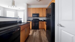Eine moderne Küche mit Holzschränken, einem schwarzen Kühlschrank, einer Mikrowelle und einem Geschirrspüler.