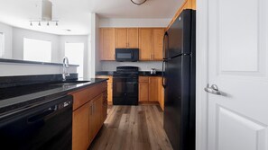 Eine moderne Küche mit Holzschränken, einem schwarzen Kühlschrank, einer Mikrowelle und einem Geschirrspüler.