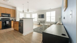 Una cucina moderna con forno a microonde, piano cottura e lavastoviglie. C'è un'area pranzo con tavolo e sedie, e un soggiorno con divano e televisione.