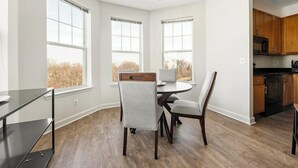 A modern kitchen with wooden cabinets, a black refrigerator, and a dining area with a round table and four chairs. - Landing | Stunning 2BD, Gym, Pool (Frederick)