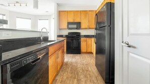 A modern kitchen with wooden cabinets, a black refrigerator, a microwave, and a dishwasher. - Landing | Stunning 2BD, Gym, Pool (Frederick)