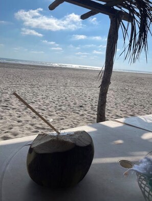 A beach scene with a coconut drink on a table, a palm tree, and the ocean in the background.