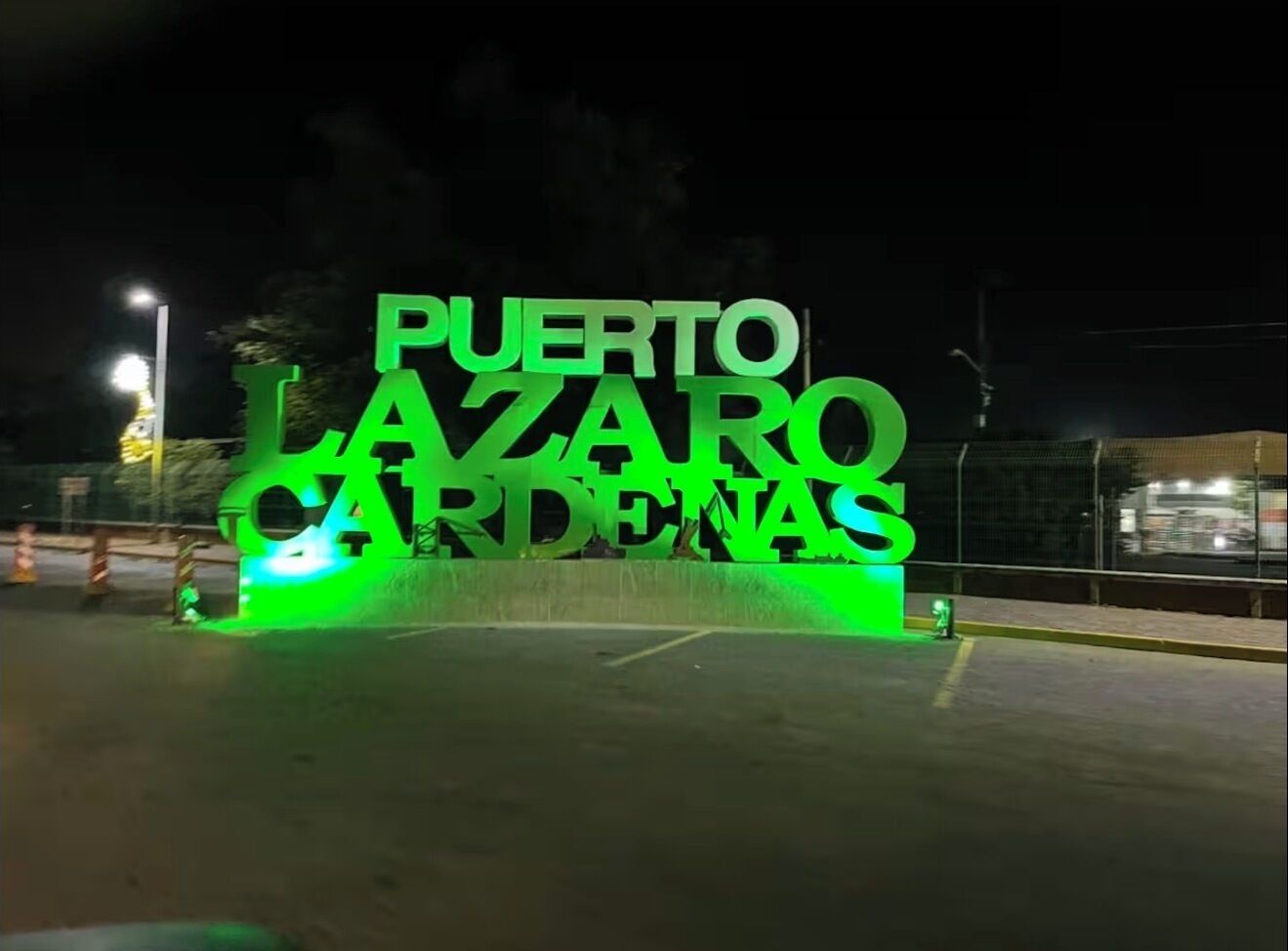 Ein Nachtbild eines Schildes mit der leuchtend grünen Aufschrift 'Puerto Lázaro Jardines'.