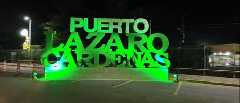 Ein Nachtbild eines Schildes mit der leuchtend grünen Aufschrift 'Puerto Lázaro Jardines'.