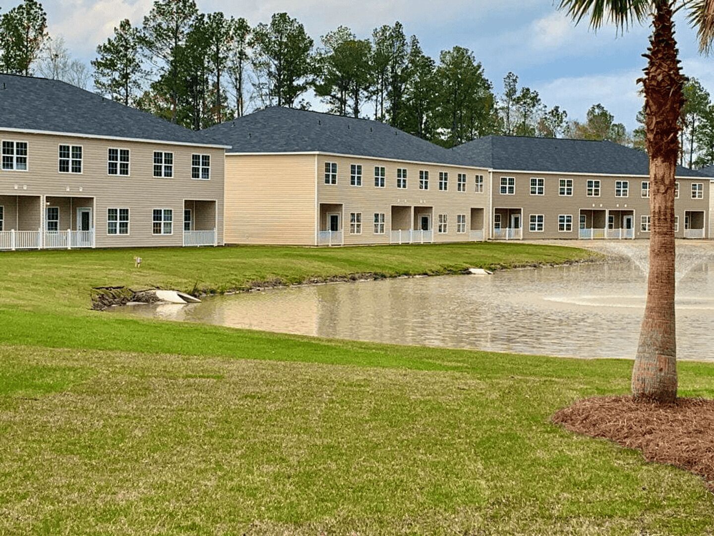 A multi-story building with a flat roof, a grassy lawn, and a small pond.