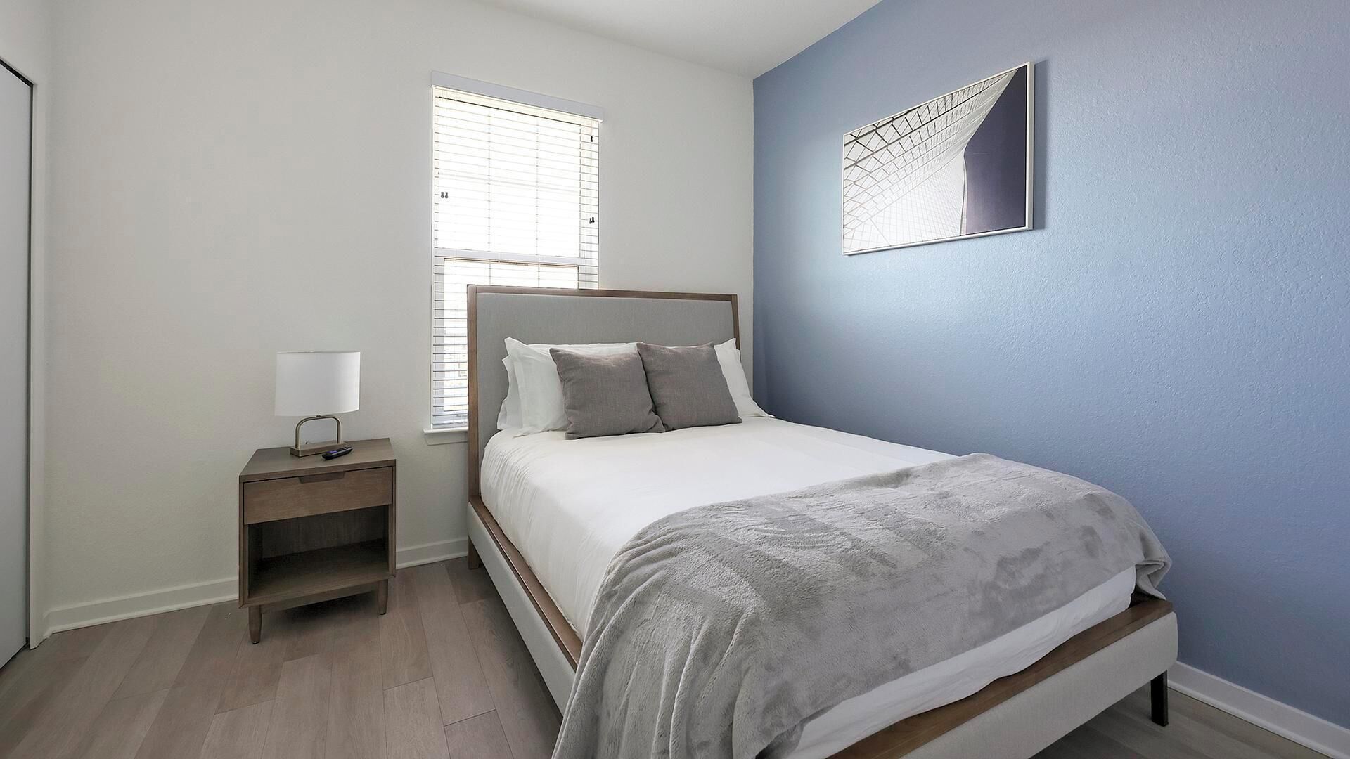 A bedroom with a bed, a bedside table with a lamp, and a window with blinds.