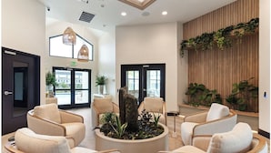 Um lobby moderno com assentos, um arranjo de plantas central e uma parede de madeira com vegetação.