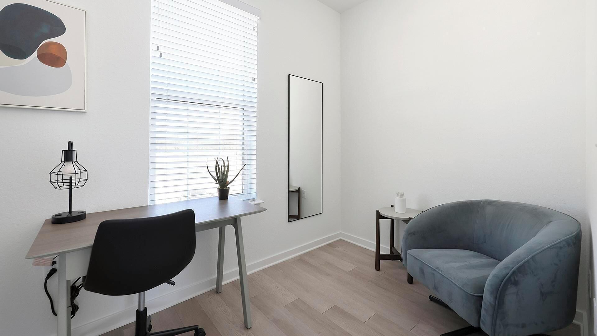 Une pièce moderne et minimaliste, équipée d’un bureau, d’une chaise et d’un fauteuil bleu.