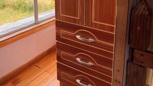 A wooden wardrobe with mirrored doors and drawers, positioned next to a window with a view of a forest and mountains. - Giardino Cabins in Lago Ranco (Lago ranco)
