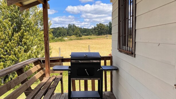 A covered outdoor area with a barbecue grill, wooden benches, and a view of a field. - Giardino Cabins in Lago Ranco (Lago ranco)