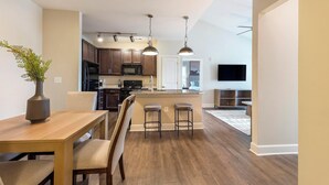 A modern kitchen with dark wood cabinets, a granite countertop, and stainless steel appliances. There is a dining area with a wooden table and chairs, and a bar area with stools. - Landing | Modern 2BD, Clubhouse, Gym (Greer)