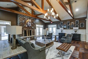 A spacious living room with a stone fireplace, wooden beams, and a chandelier. There are multiple seating areas with sofas and a coffee table. - Landing | Modern 2BD, Clubhouse, Gym (Greer)