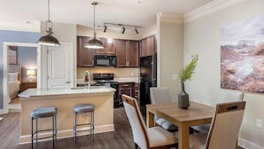 A modern kitchen with dark wood cabinets, stainless steel appliances, and a central island with bar stools. - Landing | Spectacular 2BD, Clubhouse, Gym (Greer)
