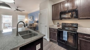 A kitchen with granite countertops, a stainless steel sink, a black oven, and dark wooden cabinets. - Landing | Spectacular 2BD, Clubhouse, Gym (Greer)