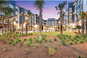 A modern hotel with multiple floors, outdoor seating areas, and palm trees. - Landing | Chic 1BD, Yoga Studio, Game Room (Bellview)
