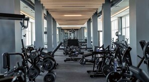 A gym with various exercise equipment, a central mirror, and a long corridor with large windows. - Landing | Beautiful 1BD, Gym, Rooftop Lounge (Bellview)