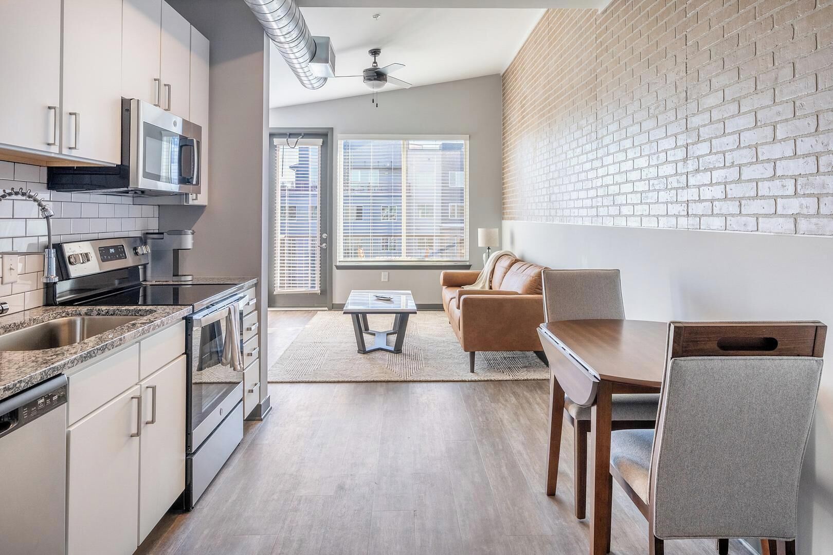 Een moderne keuken met roestvrijstalen apparatuur, een eethoek met een houten tafel en stoelen, en een met baksteen beklede muur.