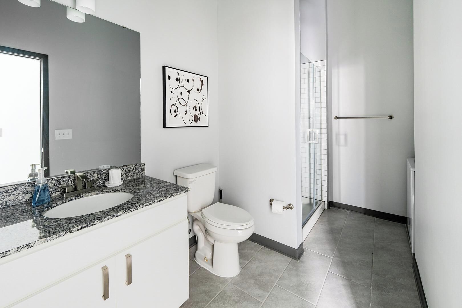 A modern bathroom with a granite countertop sink, a toilet, and a glass shower enclosure.