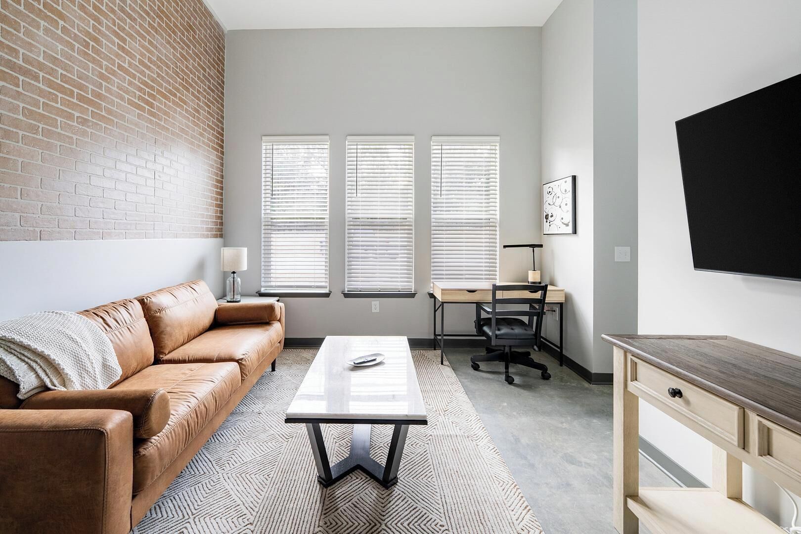 Un salon moderne avec un canapé en cuir, une table basse, un bureau avec une chaise et un téléviseur fixé au mur.