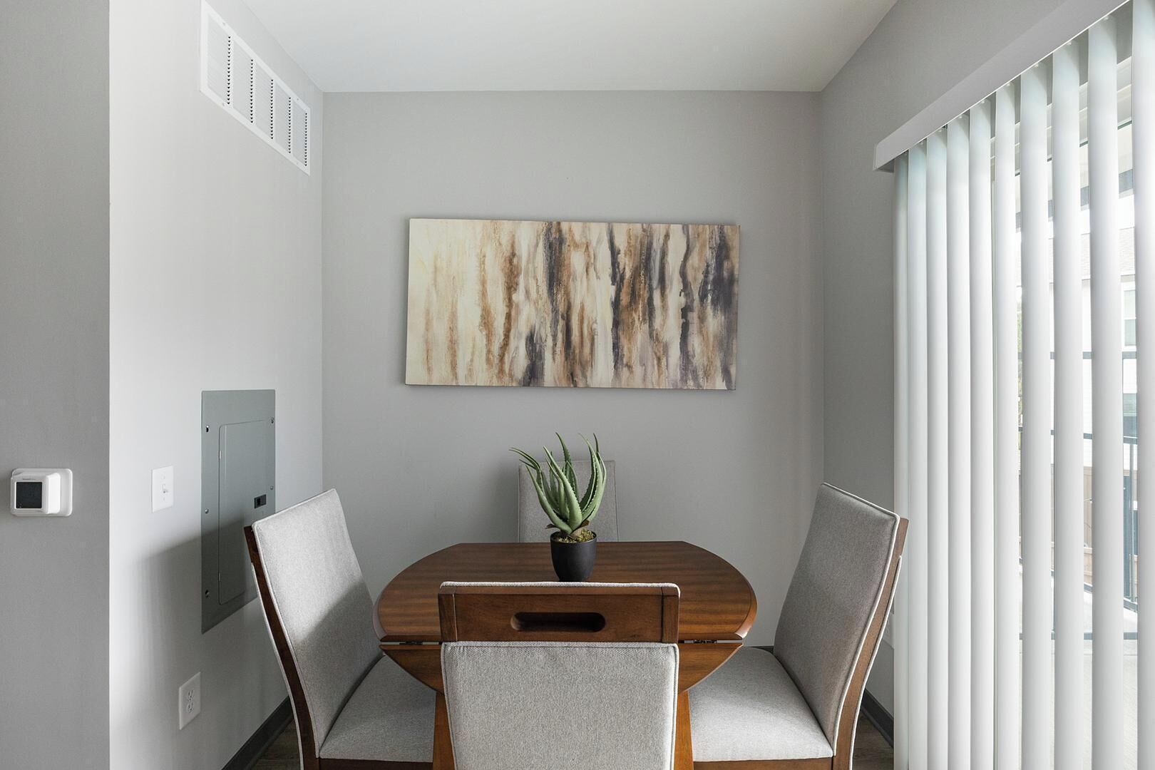 Un comedor moderno con una mesa de madera, dos sillas, una planta en maceta y un cuadro abstracto grande en la pared.