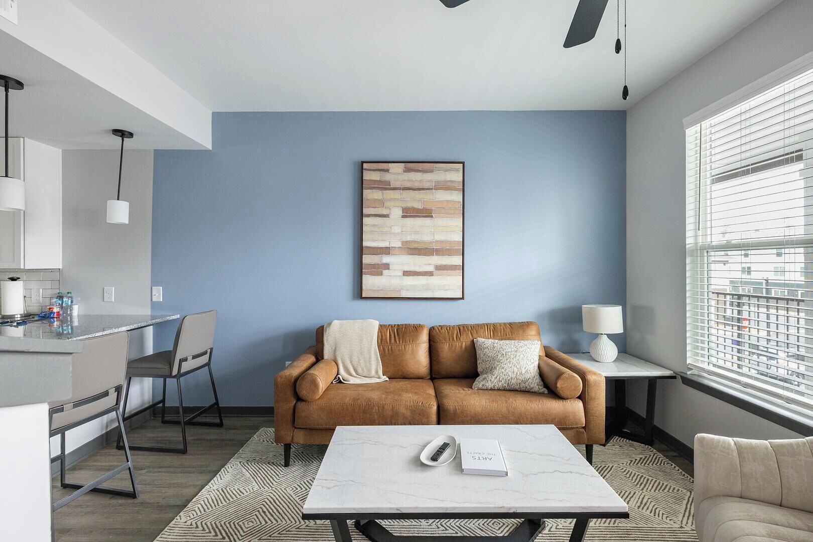 A modern living room with a brown leather sofa, a white coffee table, and a painting on the wall.