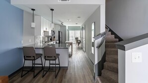 A modern kitchen with a central island, bar stools, and a staircase leading to another level. - Landing | Modern 2BD, Gym, Rooftop Lounge (Bellview)