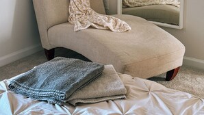 Ein Zimmer mit einem einzelnen Sessel, einem großen Spiegel und einem Bett mit weißer Bettdecke.