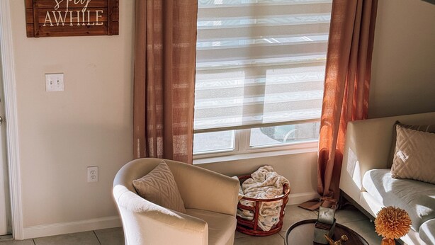 Ein Wohnzimmer mit einer Couch, Sesseln, einem Couchtisch und einem Fenster mit Vorhängen.