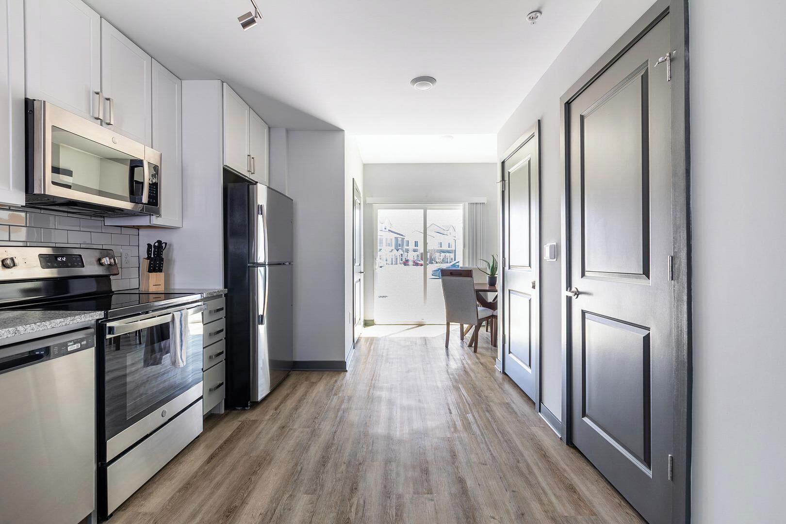 A modern kitchen with stainless steel appliances, a wooden floor, and a view to the outside.