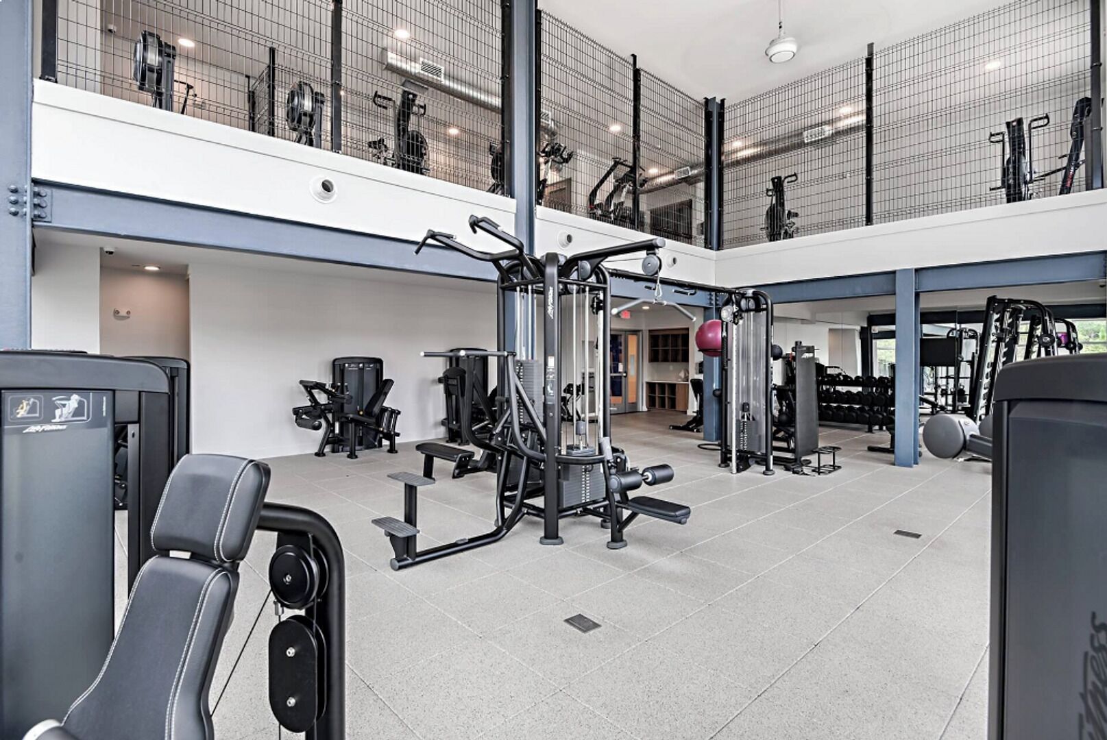 Une salle de sport à plusieurs niveaux, équipée de divers appareils d’exercice, d’un banc de musculation et d’un mur recouvert de miroirs.