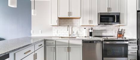 A modern kitchen with white cabinets, a granite countertop, stainless steel appliances, and a wooden floor.