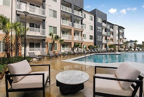 A hotel pool area with lounge chairs and a table, surrounded by multi-story buildings with balconies.