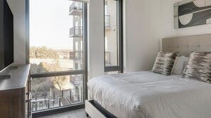 A bedroom with a large window, a bed with pillows, a TV, and a wall-mounted artwork. - Landing | Amazing 2BD in Uptown Charlotte (Charlotte)