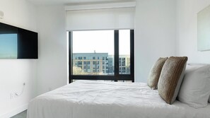 A bedroom with a large window, a bed with white bedding, and a view of buildings outside. - Landing | Amazing 1BD in Uptown Charlotte (Charlotte)