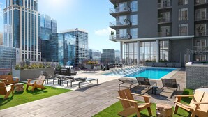 Un espace piscine aménagé sur le toit, avec des chaises longues, un jacuzzi et une vue sur les immeubles environnants.