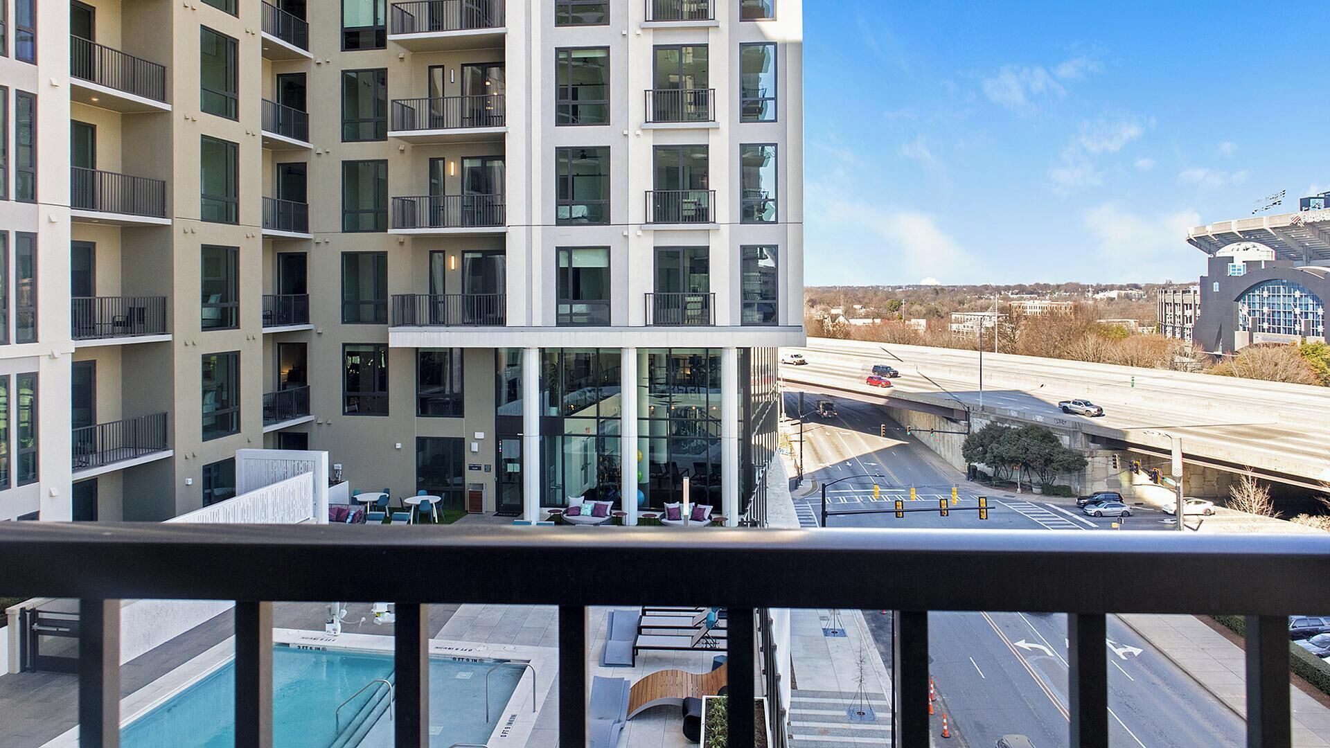 Un edificio de varios pisos con balcones, piscina en la azotea y vistas a una autopista y al paisaje urbano.