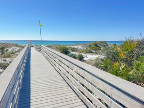 A wooden boardwalk leading to a beach with a flag, clear blue sky, and ocean view. - Beach & Lake!!! 2 King Beds Condo - in PCB - Private Boat Launch & Fishing Pier (Panama City Beach)