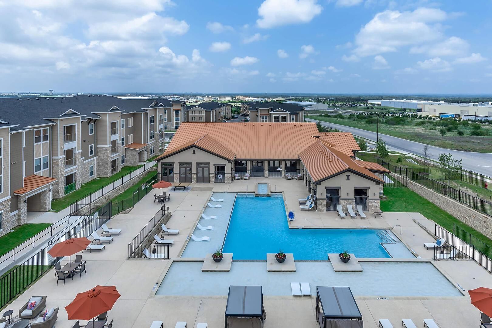 A hotel with a large outdoor pool, lounge chairs, and a patio area.