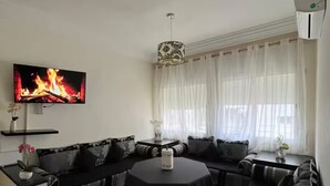 Ein modernes Wohnzimmer mit einer schwarzen Sofagarnitur, einem runden Couchtisch und einem Flachbildfernseher, der einen Kamin zeigt.