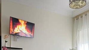 Ein Wohnzimmer mit einer Couch, einem Couchtisch, einem Fernseher, der ein Feuer zeigt, und einer Vase mit Blumen.