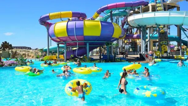 Ein Wasserpark mit mehreren Wasserrutschen und Personen, die im Pool mit aufblasbaren Ringen spielen.