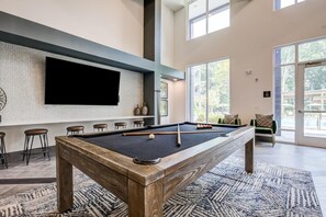 A pool table with a wooden frame, a mounted television, and a bar area with stools.