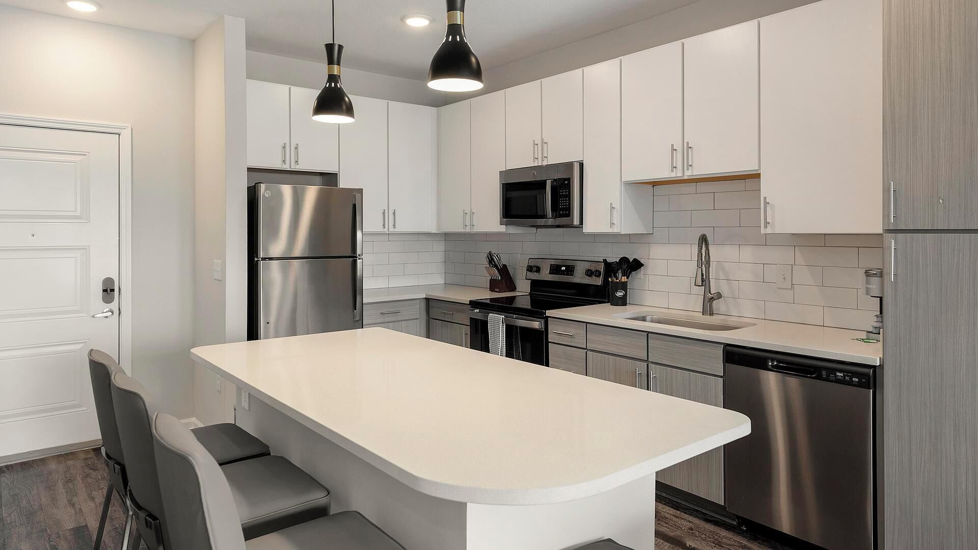 Una cocina moderna con armarios blancos, electrodomésticos de acero inoxidable, una isla central con asientos e iluminación colgante.