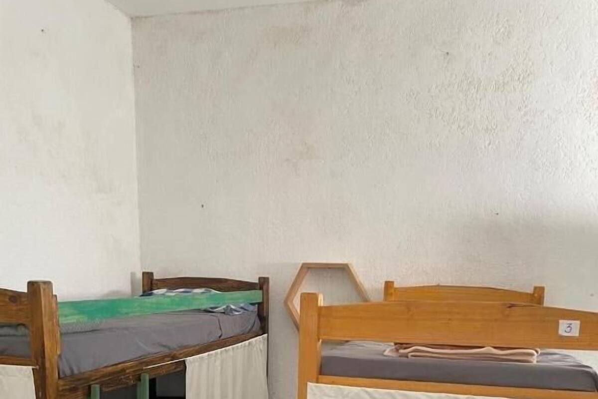 A dormitory room with two wooden bunk beds, each with a mattress and a white sheet.