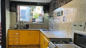 Une cuisine de taille réduite avec des meubles de couleur jaune, une cuisinière en acier inoxydable et une fenêtre donnant sur la rue.