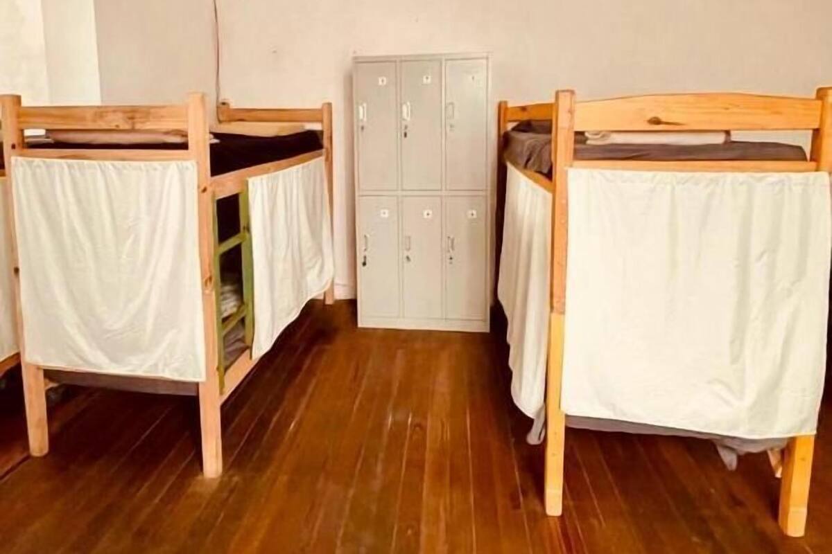 A dormitory room with two wooden bunk beds, a wardrobe, and a wardrobe with multiple doors.