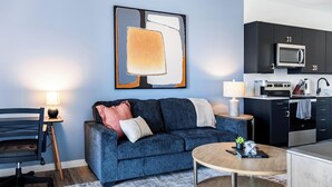 Una sala de estar moderna con un sofá azul, una mesa de centro redonda y un cuadro en la pared.