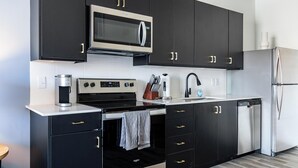 Una cocina moderna con gabinetes negros, electrodomésticos de acero inoxidable y encimera blanca.
