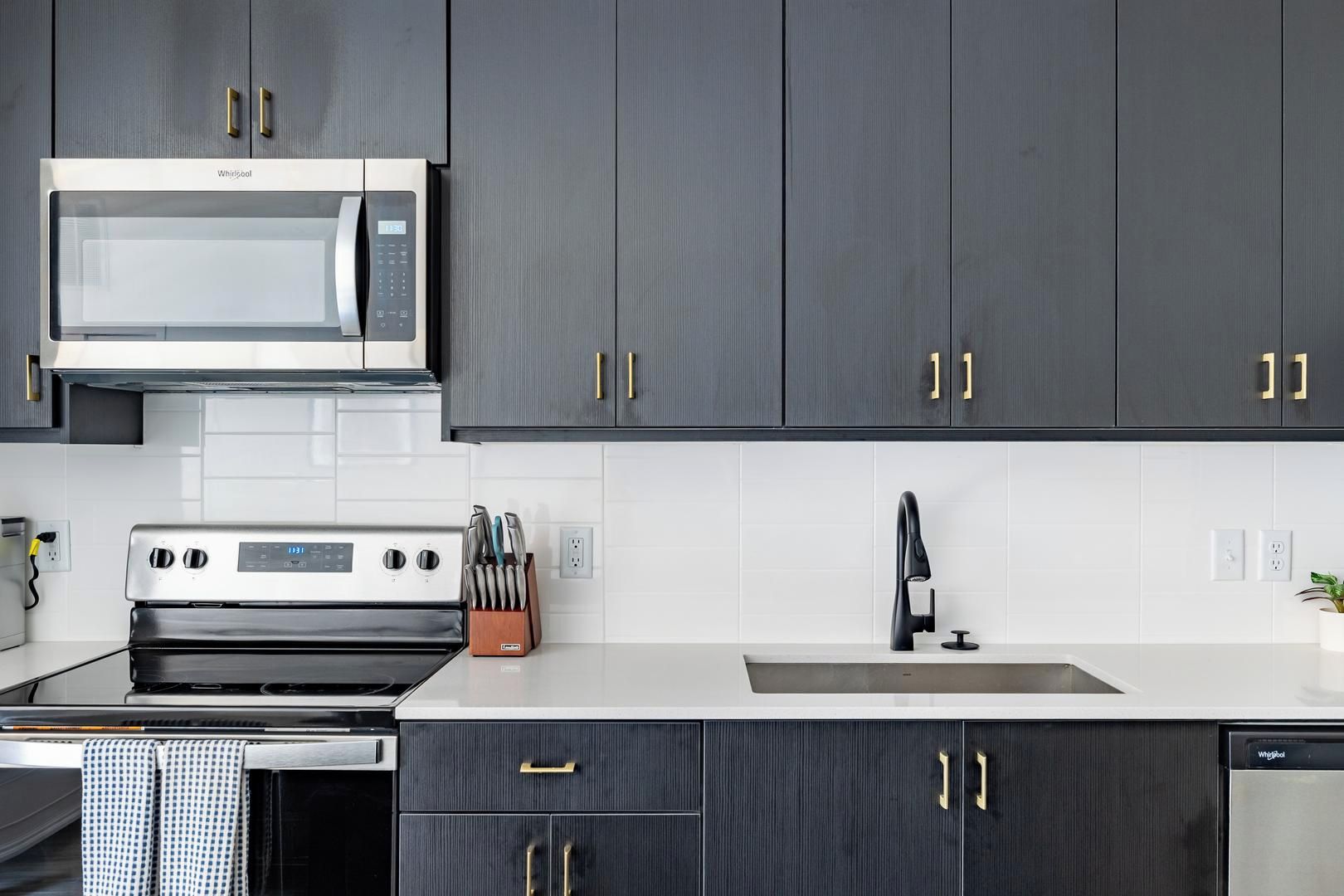 Une cuisine moderne avec des meubles de couleur sombre, un four à micro-ondes, une cuisinière et un lave-vaisselle.